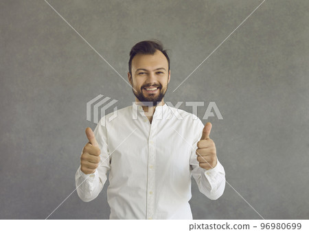 Portrait of happy young man giving thumbs up standing isolated on grey background 96980699