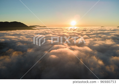 Aerial view of colorful sunrise over white dense fog with distant dark silhouettes of mountain hills on horizon Aerial view of colorful sunrise over white dense fog with distant dark silhouettes of mountain hills on horizon 96980753