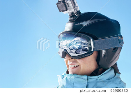 Skier with action camera on a helmet. Ski goggles  with the reflection of snowed mountains. Portrait of man at the ski resort on the background of mountains and blue sky,. Wearing ski glasses 96980880