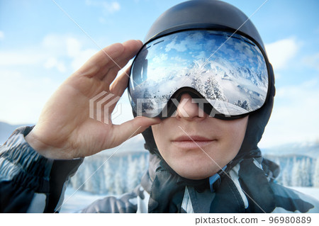 Close Up Of The Ski Goggles Of A Man With The Reflection Of Snowed Mountains. Man On The Background Blue Sky. Wearing Ski Glasses. Winter Sports. Close Up Of The Ski Goggles Of A Man With The Reflection Of Snowed Mountains. Man On The Background Blue Sky. Wearing Ski Glasses. Winter Sports. 96980889