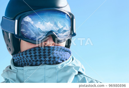 Close up of the ski goggles of a man with the reflection of snowed mountains.  A mountain range reflected in the ski mask.  Portrait of man at the ski resort.  Wearing ski glasses. Winter Sports. 96980896