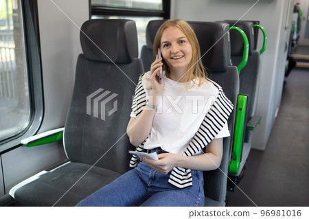 Young blonde 20s 30s woman call using smart phone in speed train. Travel to vacation by fast train. Happy girl talking on the mobile phone. 96981016