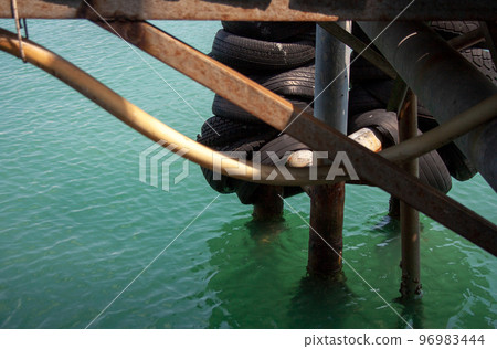 Pier detail with stacked rubber wheel tires hanging on piles above sea water 96983444