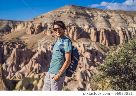 Young man exploring valley with rock formations and fairy caves near Goreme in Cappadocia Turkey Young man exploring valley with rock formations and fairy caves near Goreme in Cappadocia Turkey 96983851