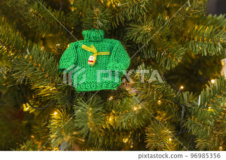 Small knitted green sweater and garlands, craft decor on branches of Christmas tree. Christmas and new year 96985356
