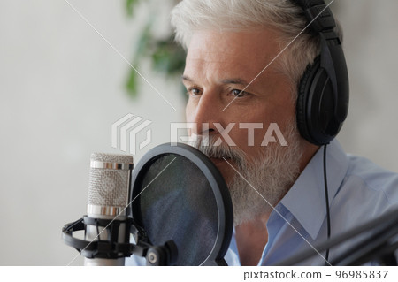 older man with gray hair irecording podcast in recording studio with microphone and headphones 96985837
