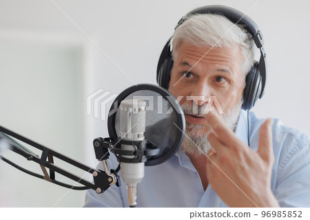 older man with gray hair irecording podcast in recording studio with microphone and headphones 96985852