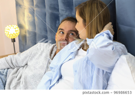 White Caucasian man looks at his pregnant woman with big belly, first baby movement while lying on bed in bedroom. Happy parenthood, child expectation. Magic moments, baby delivery White Caucasian man looks at his pregnant woman with big belly, first baby movement while lying on bed in bedroom. Happy parenthood, child expectation. Magic moments, baby delivery 96986653