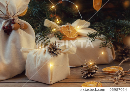 Zero waste christmas concept. Packed in natural fabric gifts and decorations from natural materials with christmas lights on a wooden table 96987034