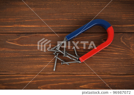 Horseshoe magnet attracting nails on wooden table, flat lay 96987072