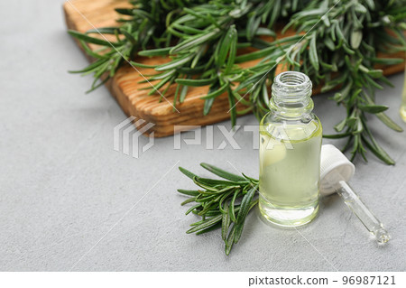 Fresh rosemary and bottle of essential oil on light grey table. Space or text 96987121