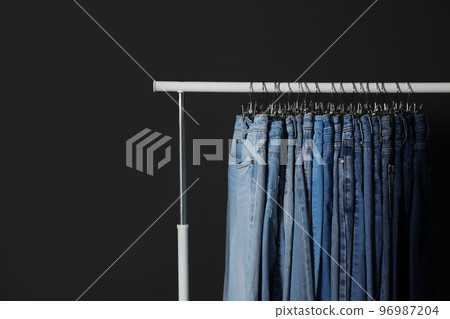 Rack with different jeans on dark grey background Rack with different jeans on dark grey background 96987204