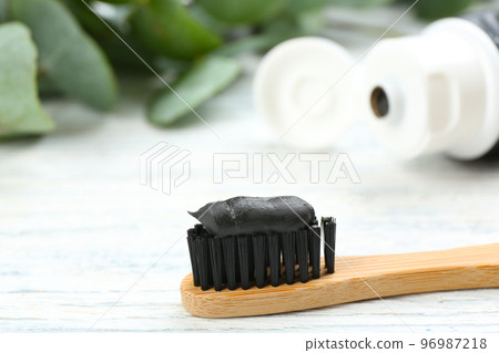 Bamboo toothbrush with charcoal paste on white wooden table, closeup. Space for text 96987218