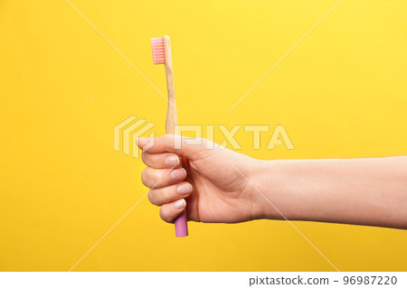 Woman holding bamboo toothbrush on yellow background, closeup 96987220