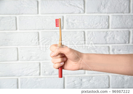 Woman holding bamboo toothbrush against white brick wall, closeup 96987222