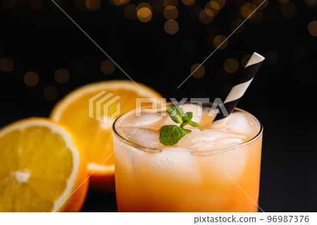 Fresh alcoholic Tequila Sunrise cocktail against blurred lights, closeup Fresh alcoholic Tequila Sunrise cocktail against blurred lights, closeup 96987376
