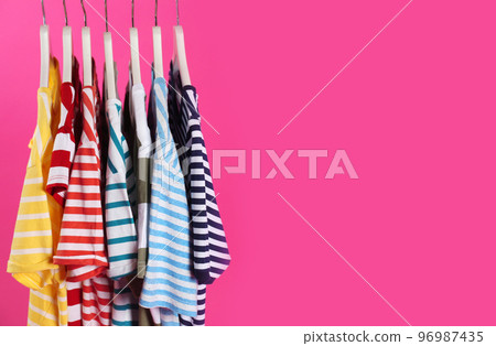 Colorful clothes on hangers against pink background, space for text Colorful clothes on hangers against pink background, space for text 96987435