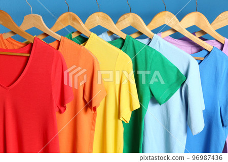 Bright clothes on wooden hangers against blue background. Rainbow colors 96987436