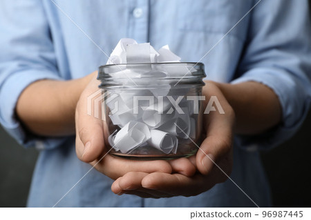 Woman holding glass jar with paper pieces, closeup on hands Woman holding glass jar with paper pieces, closeup on hands 96987445