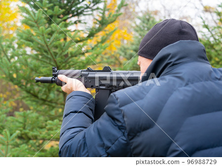 A man carefully aims from a machine gun, pressing the butt to his shoulder 96988729