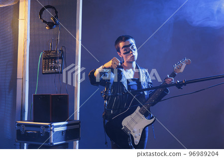 Mad crazy rocker showing clenched fist in studio with smoke, acting violent and being aggressive. Heavy metal artist singing alternative music with guitar, being angry and making threat. 96989204