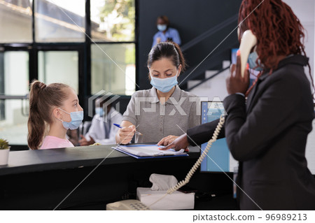 Kid waiting mother to sign medical insurance papers standing at reception desk during checkup visit consultation in hospital lobby. People wearing protective face mask to against covid19 Kid waiting mother to sign medical insurance papers standing at reception desk during checkup visit consultation in hospital lobby. People wearing protective face mask to against covid19 96989213