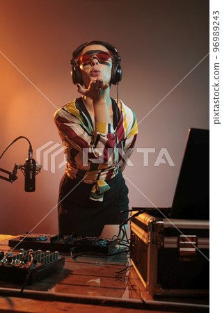 Woman DJ blowing air kisses in studio, being romantic and acting flirty while she mixes techno music at turntables. Charming dreamy artist trying to remix song at electric mixer. 96989243