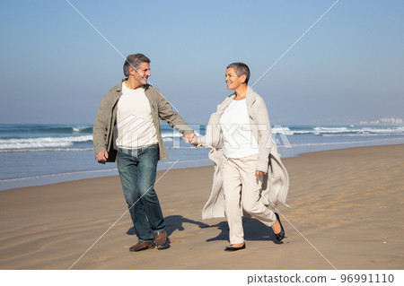 Happy senior couple walking along seashore Happy senior couple walking along seashore 96991110
