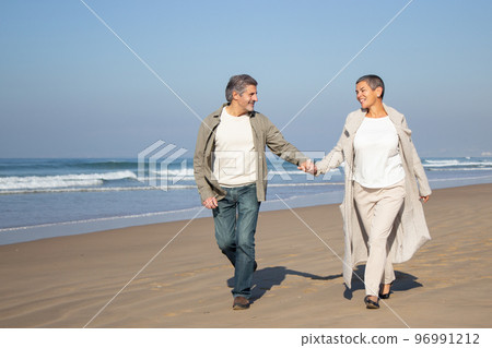 Senior couple walking along seashore 96991212