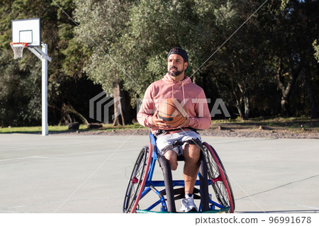 Bearded man in sports wheelchair holding orange basketball 96991678