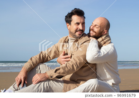 Smiling bald man sitting on sand with boyfriend 96991679
