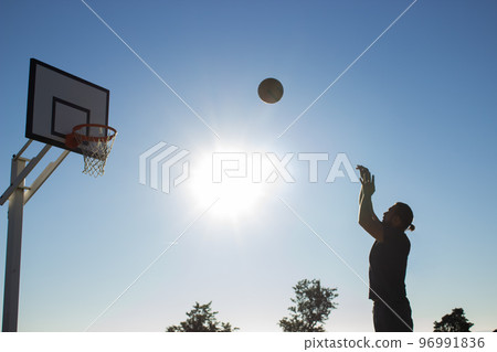 Tall man playing basketball alone on sunny day outdoors 96991836