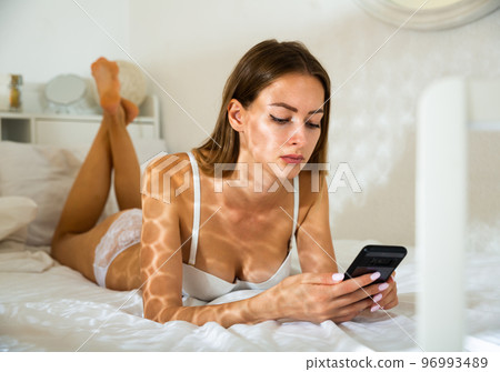 Girl texting on phone in bed 96993489