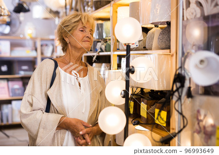 Mature woman choosing new lamp at shop Mature woman choosing new lamp at shop 96993649