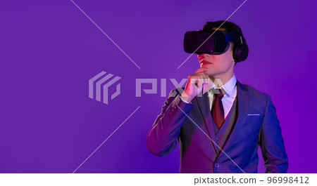 Asian businessman in white shirt red tie and jacket suit wear vr glasses virtual reality headset posing watching thinking on purple color background. Asian businessman in white shirt red tie and jacket suit wear vr glasses virtual reality headset posing watching thinking on purple color background. 96998412