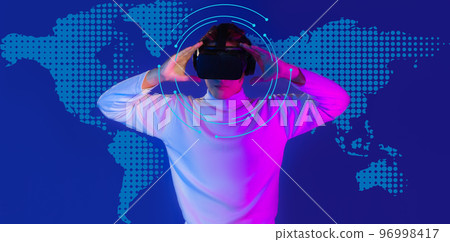 Asian man in white long sleeve t shirt wear vr virtual reality goggles headset posing with hologram blue color background. Asian man in white long sleeve t shirt wear vr virtual reality goggles headset posing with hologram blue color background. 96998417
