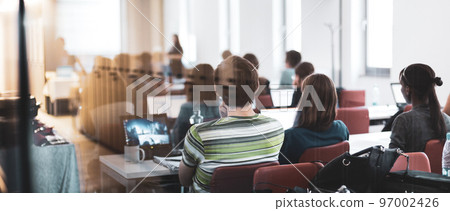 Workshop at university. Rear, trough the window, view of students sitting and listening in lecture hall doing practical tasks on their laptops. 97002426