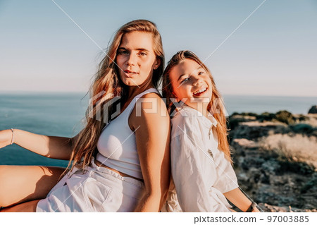 Sea family vacation together, happy mom and teenage daughter hugging and smiling together over sunset sea view. Beautiful woman with long hair relaxing with her child. Concept of happy friendly family 97003885
