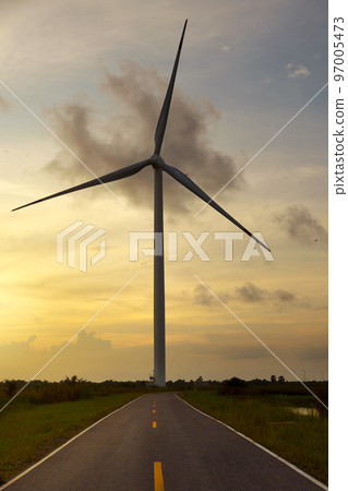 Wind turbine standing by the road against a sunset sky and a green meadow. Wind turbine standing by the road against a sunset sky and a green meadow. 97005473