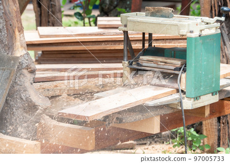 Joiner, Man's hand scouring a wooden board on a thickness machine in garden. Carpenter working with electric planer on wooden beam, plank.DIY concept Joiner, Man's hand scouring a wooden board on a thickness machine in garden. Carpenter working with electric planer on wooden beam, plank.DIY concept 97005733