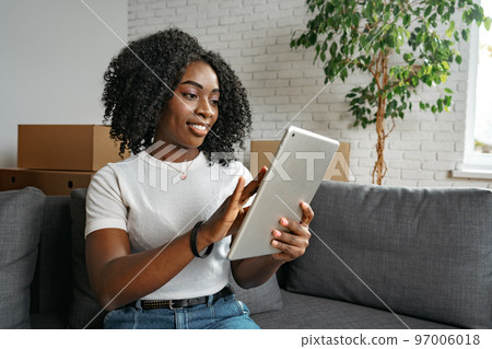 Young african woman using digital tablet and smiling while resting at home. 97006018