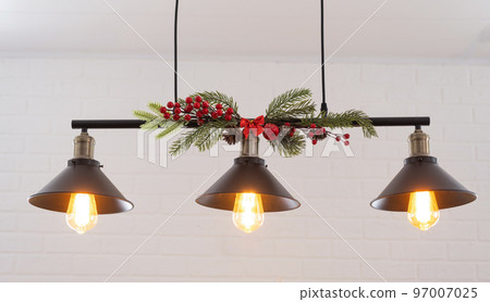 The black lampshade in the industrial loft style is decorated with spruce branches for Christmas and New Year on the background white brick wall. Close-up, minimalism 97007025