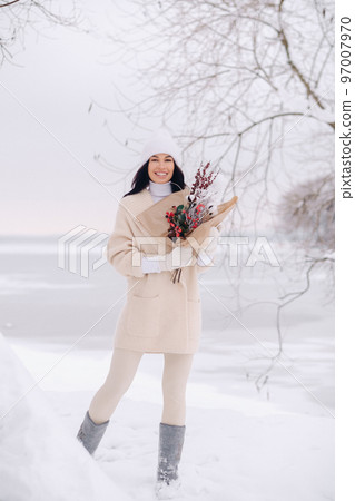 A girl in a beige cardigan and winter flowers walks in nature in the snowy season. Winter weather A girl in a beige cardigan and winter flowers walks in nature in the snowy season. Winter weather 97007970