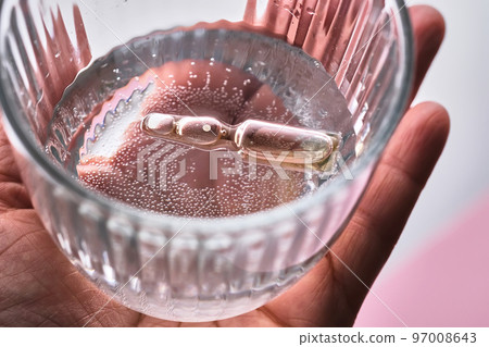 Ampoule in a mug with water on a pink background. The symbol of humidification. 97008643