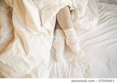 Legs in warm leggings and wool socks peek out from under the blanket. Legs in warm leggings and wool socks peek out from under the blanket. 97008663