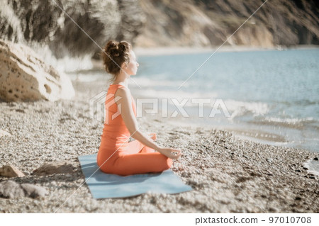 Woman sea yoga. Selective focus. Young beautiful caucasian woman in a red suit practicing yoga on the beach at sunrise near the sea. Yoga. Healthy lifestyle. Meditation concept. Woman sea yoga. Selective focus. Young beautiful caucasian woman in a red suit practicing yoga on the beach at sunrise near the sea. Yoga. Healthy lifestyle. Meditation concept. 97010708