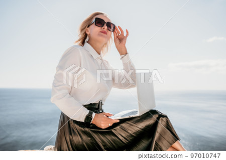 Digital nomad, Business woman working on laptop by the sea. Pretty lady typing on computer by the sea at sunset, makes a business transaction online from a distance. Freelance, remote work on vacation Digital nomad, Business woman working on laptop by the sea. Pretty lady typing on computer by the sea at sunset, makes a business transaction online from a distance. Freelance, remote work on vacation 97010747