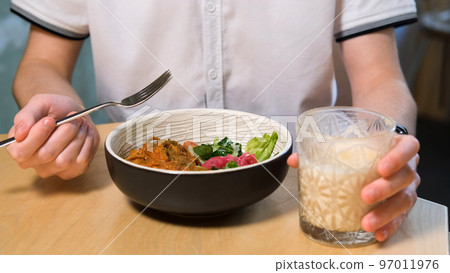 Young male eating delicious fettuccine pasta with tomato sauce and vegetables while drinking vegan latte drink at cafe or restaurant 97011976