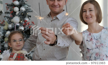Family of three holding sparklers while celebrating Xmas or New year at home, selective focus Family of three holding sparklers while celebrating Xmas or New year at home, selective focus 97011983
