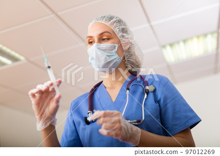 Female doctor in mask preparing syringe for vaccination Female doctor in mask preparing syringe for vaccination 97012269